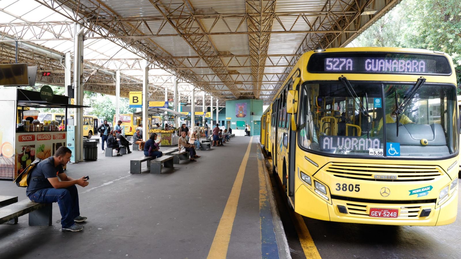 Ônibus amarelo da linha 527A no Terminal Central de Jundiaí, com passageiros aguardando nas plataformas sob cobertura metálica.