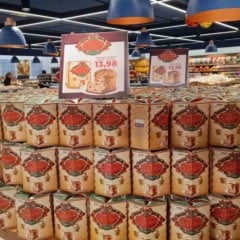 Empilhamento de panetones da campanha Panetone Solidário Tauste com cartaz exibindo o preço de R$ 13,98 dentro de um supermercado.