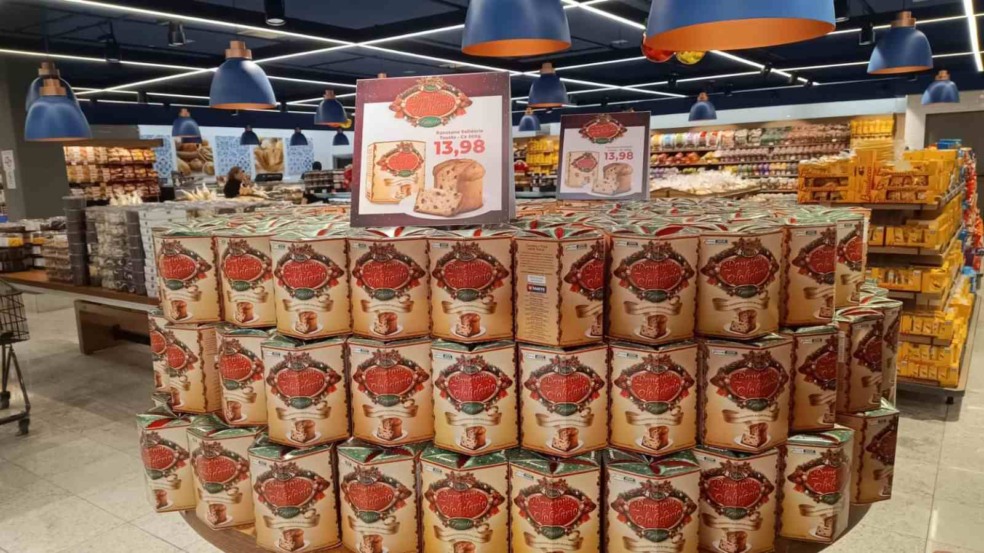 Empilhamento de panetones da campanha Panetone Solidário Tauste com cartaz exibindo o preço de R$ 13,98 dentro de um supermercado.