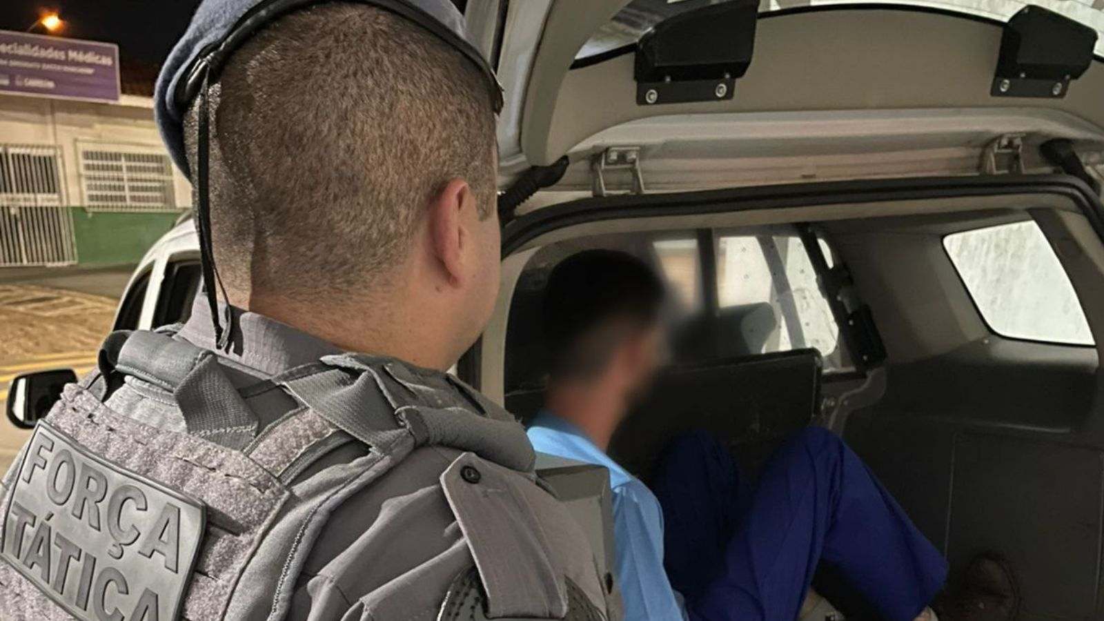 Policial da Força Tática observa um homem detido sentado no compartimento traseiro de uma viatura, durante uma ocorrência em Cabreúva (SP).