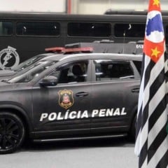 Viatura da Polícia Penal de São Paulo ao lado das bandeiras do Brasil, do Estado e do brasão da corporação.