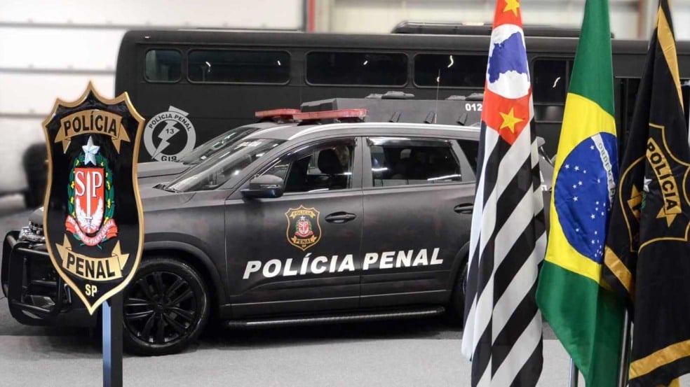 Viatura da Polícia Penal de São Paulo ao lado das bandeiras do Brasil, do Estado e do brasão da corporação. Viatura da Polícia Penal de São Paulo ao lado das bandeiras do Brasil, do Estado e do brasão da corporação.