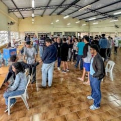 Pessoas em fila sendo atendidas por servidores públicos em ação comunitária da Prefeitura de Jundiaí, realizada em espaço coberto e iluminado.