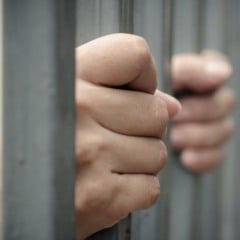 Mãos segurando as grades de uma cela, representando prisão e restrição de liberdade.