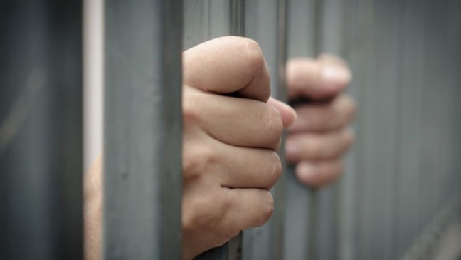 Mãos segurando as grades de uma cela, representando prisão e restrição de liberdade.