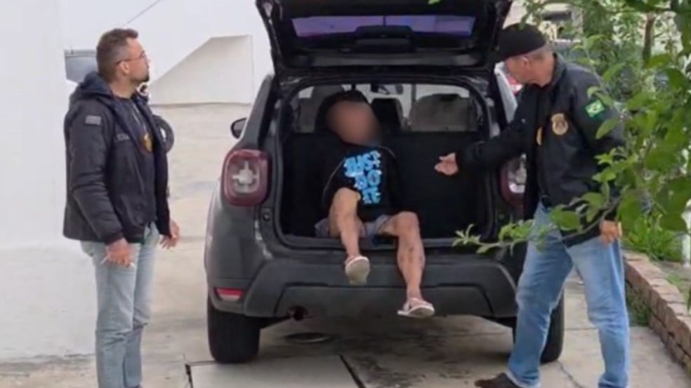 Policiais civis de Jundiaí ao lado de um carro preto com o porta-malas aberto, onde está sentado um homem detido, suspeito de envolvimento em homicídio.