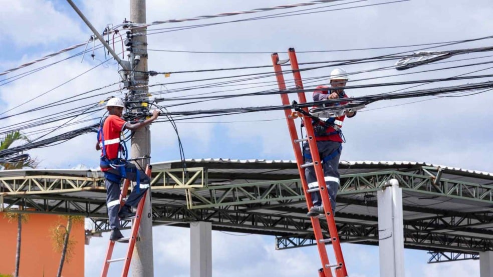 Trabalhadores em escadas reorganizando cabos em um poste, usando equipamentos de segurança, durante ação de reordenamento de fiação em Jundiaí.