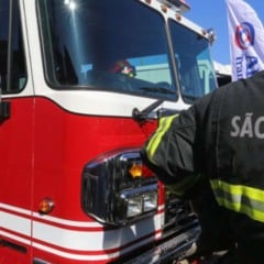 Bombeiro de São Paulo ao lado de caminhão vermelho do Corpo de Bombeiros em dia ensolarado.