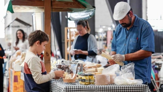 Produtor rural atende um menino em banca de queijos, pães e doces artesanais durante o evento Sabores da Gente no Espaço Expressa, em Jundiaí.