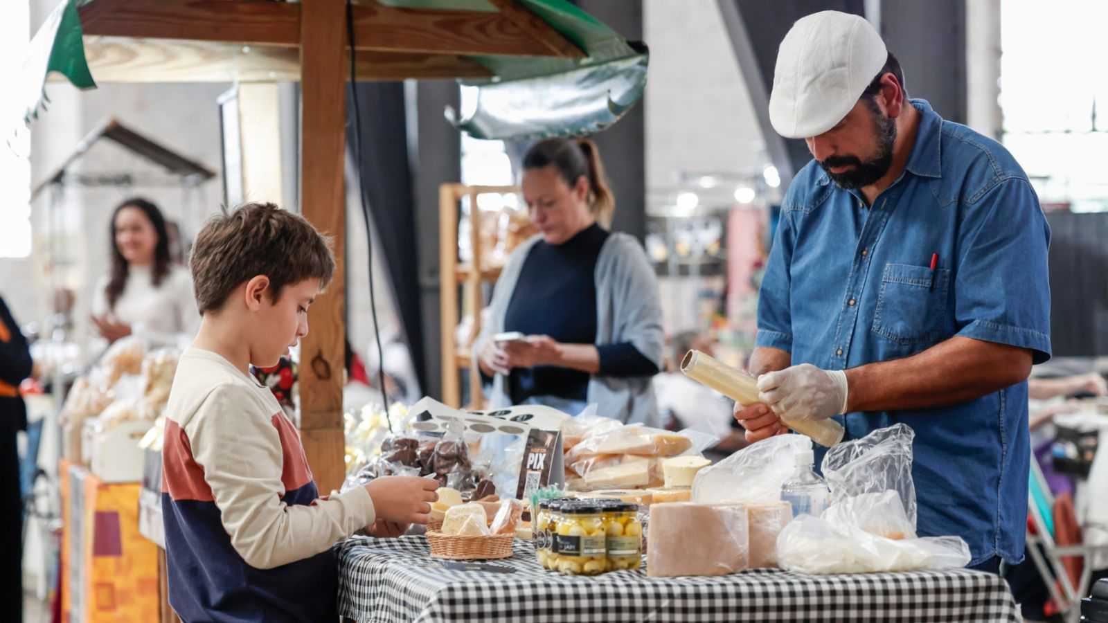 Produtor rural atende um menino em banca de queijos, pães e doces artesanais durante o evento Sabores da Gente no Espaço Expressa, em Jundiaí.