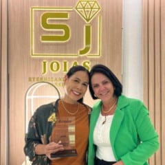 Talita e Maria Salviano posam sorrindo na loja da Salviano Jóias; Talita segura a placa de homenagem da ACE Jundiaí, com o logotipo iluminado da joalheria ao fundo.
