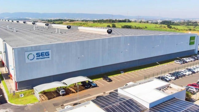 Vista aérea da fábrica da SEG Automotive em Itupeva, com galpão industrial, estacionamento e área verde ao fundo.
