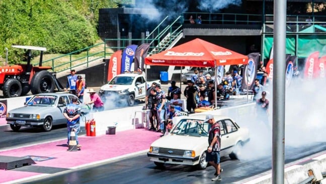 Carros de arrancada fazendo burnout na pista do SPID em Itatiba, com equipes ao redor, fumaça intensa e estrutura do evento ao fundo.