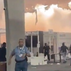Interior do Pavilhão dos Países da COP30 tomado por fumaça, com teto danificado e pessoas sendo evacuadas por agentes de segurança após incêndio.