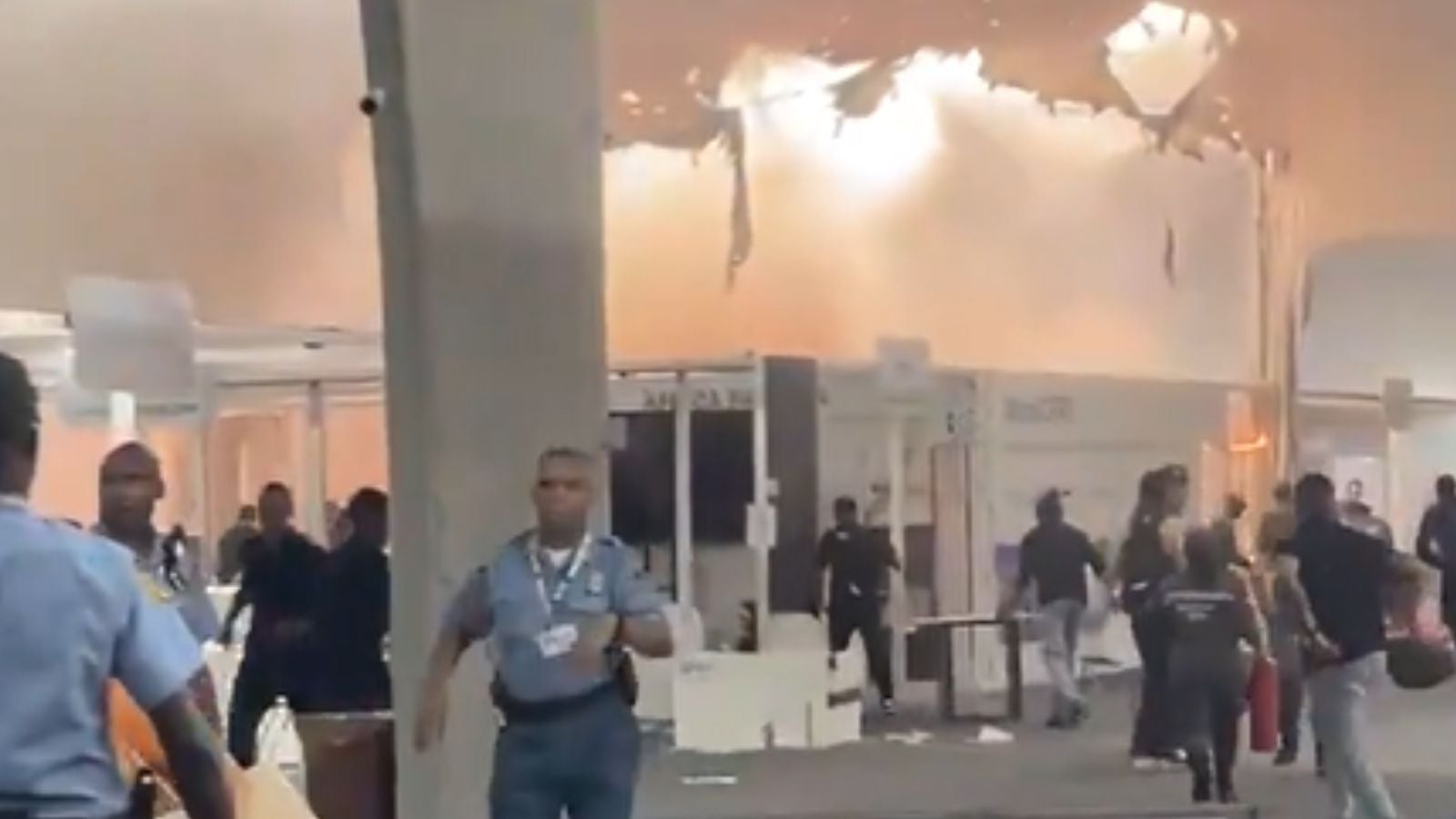 Interior do Pavilhão dos Países da COP30 tomado por fumaça, com teto danificado e pessoas sendo evacuadas por agentes de segurança após incêndio.