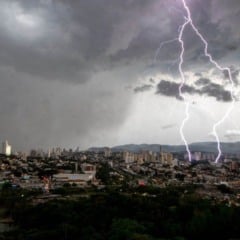 Raio atinge a cidade de Jundiaí durante uma forte tempestade, com nuvens escuras e panorama urbano ao fundo.