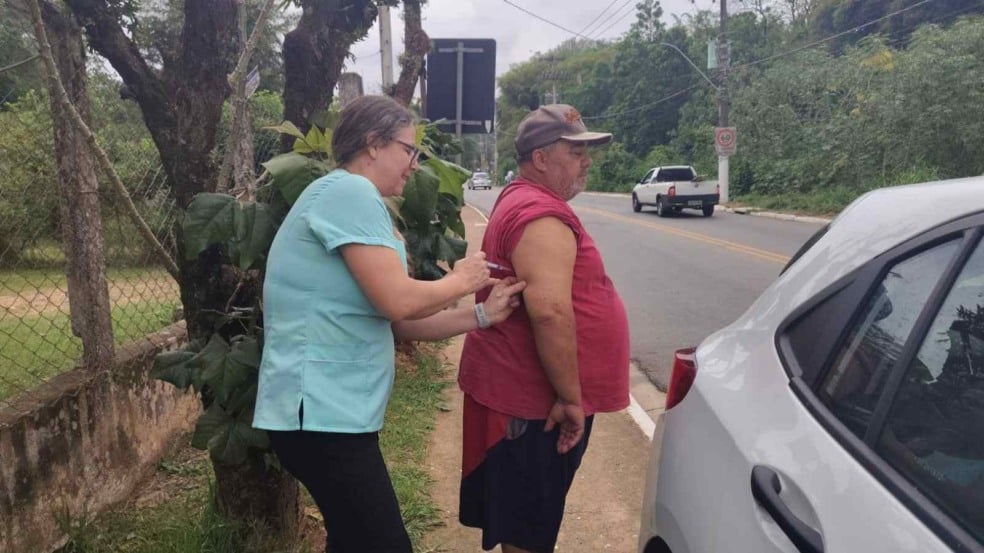 Profissional de saúde aplica vacina contra a febre amarela em um morador à beira da estrada em área rural de Jundiaí durante ação casa a casa.