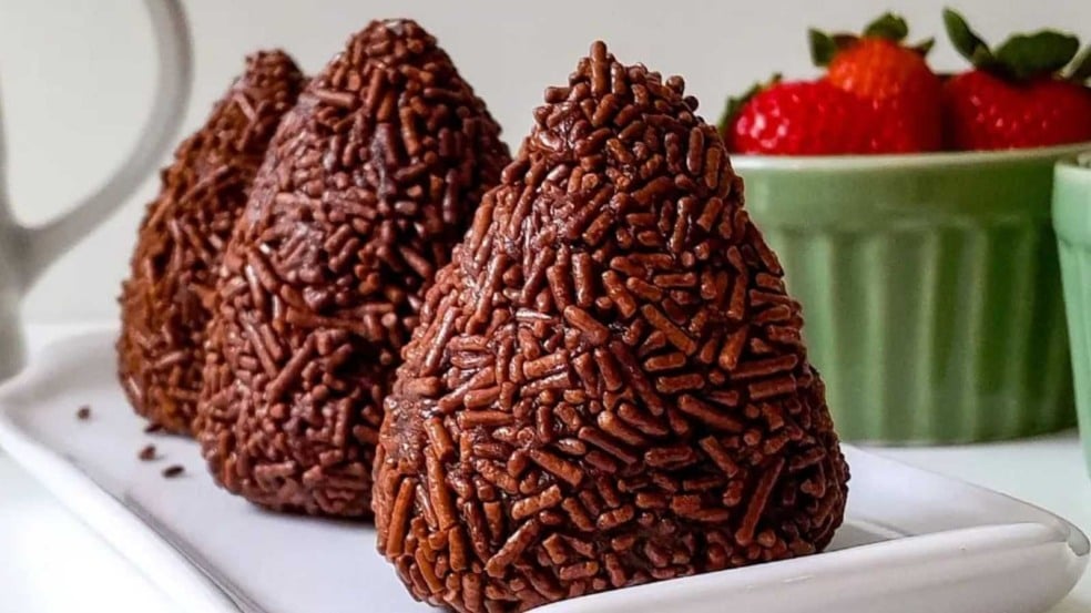 Brigadeiros veganos cobertos com granulado e acompanhados de morangos.