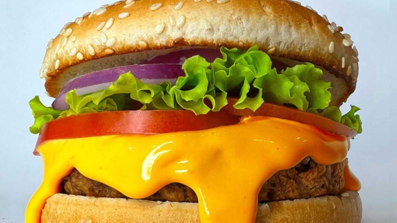 Hambúrguer vegano com queijo vegetal, alface, tomate e cebola roxa.