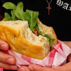Sanduíche vegano em pão artesanal com recheio vegetal e folhas verdes.
