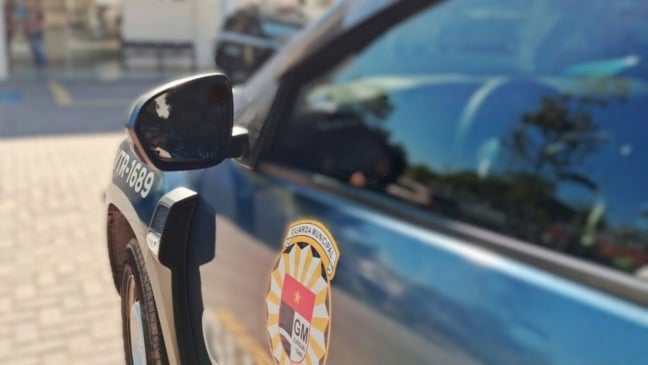 Viatura da Guarda Municipal de Jundiaí vista de perto, mostrando o brasão na porta, com o prédio do Plantão Policial desfocado ao fundo.