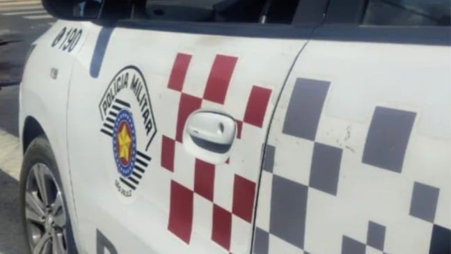 Lateral de viatura da Polícia Militar de São Paulo com brasão e padrão quadriculado, durante atendimento de ocorrência de trânsito.