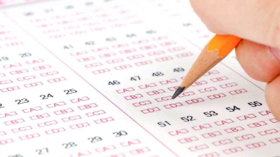 Mão preenche cartão-resposta de prova objetiva com lápis, marcando alternativa em exame de concurso público. Mão preenche cartão-resposta de prova objetiva com lápis, marcando alternativa em exame de concurso público.