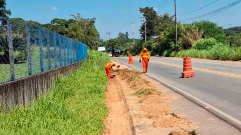 Funcionários da Prefeitura de Jundiaí, com uniformes laranja, limpam e desobstruem canaletas na Avenida da Uva, utilizando ferramentas manuais ao lado de cones de sinalização na pista. Funcionários da Prefeitura de Jundiaí, com uniformes laranja, limpam e desobstruem canaletas na Avenida da Uva, utilizando ferramentas manuais ao lado de cones de sinalização na pista.