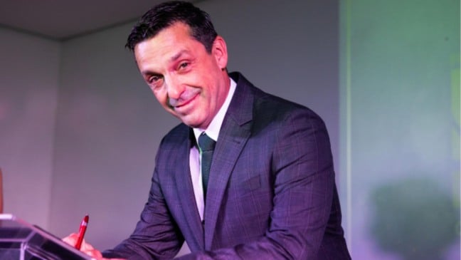 Orlando Picchi Fabrício, de terno e gravata, assina documento durante evento institucional em ambiente interno.