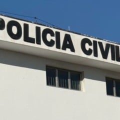 Prédio branco da Polícia Civil com letreiro em destaque e céu azul ao fundo.