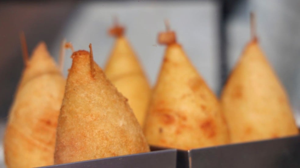 Coxinhas de queijo douradas e alinhadas em suportes metálicos, fotografadas em close com fundo desfocado. Coxinhas de queijo douradas e alinhadas em suportes metálicos, fotografadas em close com fundo desfocado.