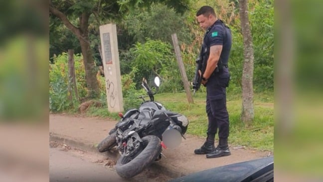 Guarda Municipal de Jundiaí observa motocicleta Kawasaki Z750 recuperada após roubo; veículo está caído na calçada em área de mata.