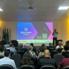 Imagem do audit&oacute;rio do CIESP Jundia&iacute; durante o Tech Day 2025, com p&uacute;blico sentado e tr&ecirc;s apresentadores no palco diante de um tel&atilde;o que mostra o logotipo do evento e um QR Code para check-in.