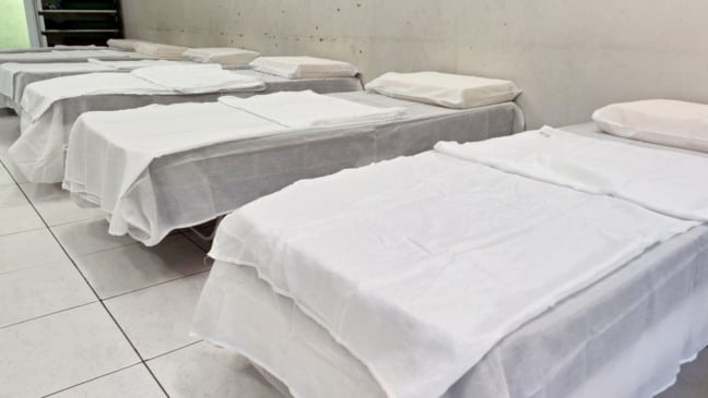 Área interna do abrigo emergencial com várias camas prontas para acolhimento de famílias.