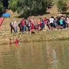 Grupo de pessoas acompanha resgate de jovem em lagoa no bairro do Jacar&eacute;, em Cabre&uacute;va, com bombeiros atuando na &aacute;gua.