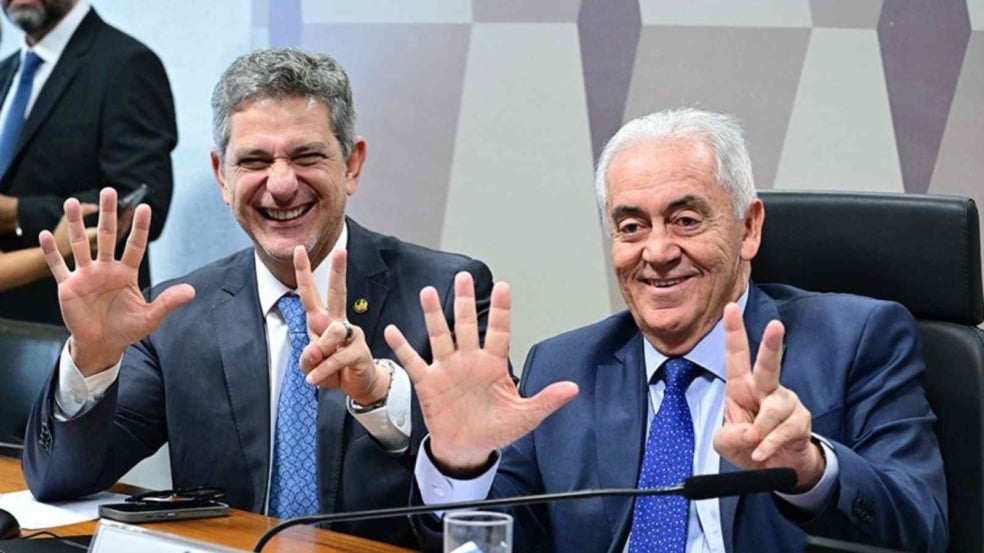 Senadores sorrindo durante sessão no Senado, fazendo com as mãos o gesto “6x2”, em referência à discussão sobre a jornada de trabalho; ambos usam terno e estão sentados lado a lado. Senadores sorrindo durante sessão no Senado, fazendo com as mãos o gesto “6x2”, em referência à discussão sobre a jornada de trabalho; ambos usam terno e estão sentados lado a lado.