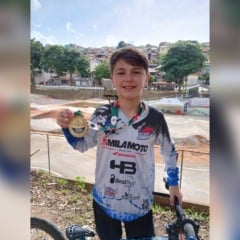 Jovem atleta de BMX Racing de Jundia&iacute; segura medalha dourada e sorri em pista de BMX ao ar livre, ao lado da bicicleta.