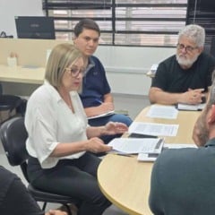Reuni&atilde;o entre equipe da FMJ e FATEC sentada ao redor de uma mesa, examinando documentos e discutindo detalhes do projeto do aplicativo.