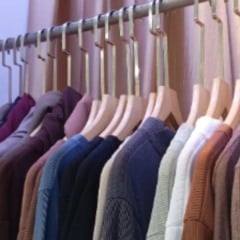 Arara com várias blusas e suéteres em tons neutros e coloridos, pendurados em cabides de madeira, organizados lado a lado.