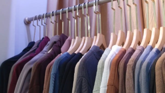 Arara com várias blusas e suéteres em tons neutros e coloridos, pendurados em cabides de madeira, organizados lado a lado.