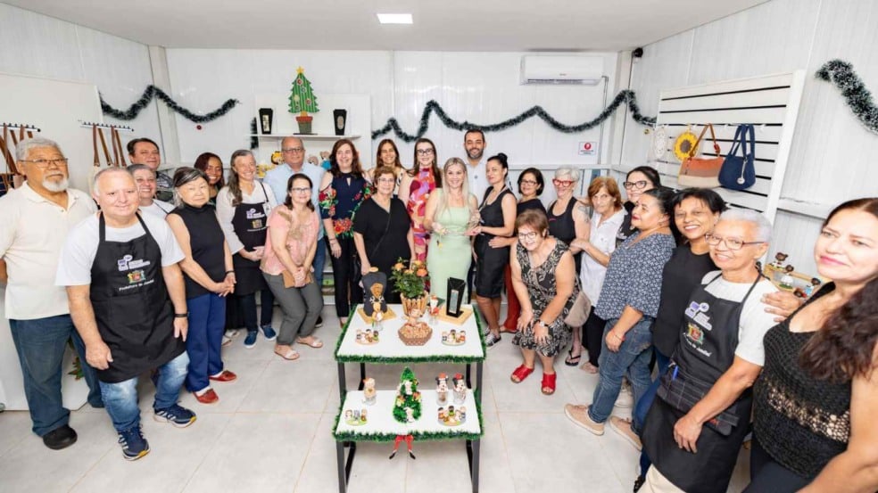Grupo de artesãos e autoridades posando juntos no interior do novo Espaço Jundiaí Feito à Mão, cercados por mesas com artesanatos natalinos e prateleiras decoradas.