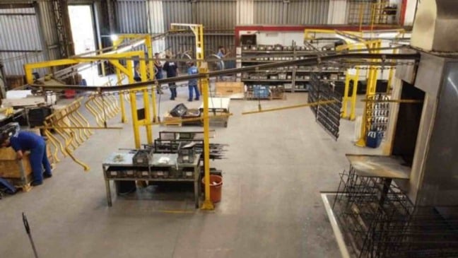 Interior de fábrica em Jundiaí mostra área de produção industrial com funcionários trabalhando, esteiras, estruturas metálicas e organização de materiais.