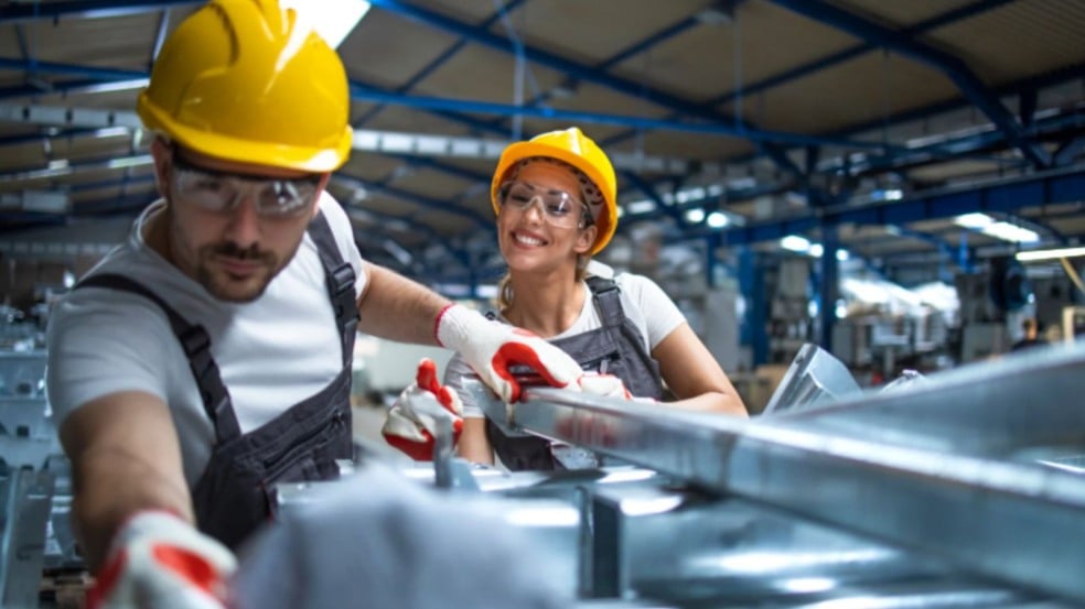 Homem e mulher usando capacetes e equipamentos de segurança trabalham juntos na montagem de peças metálicas em uma fábrica. Homem e mulher usando capacetes e equipamentos de segurança trabalham juntos na montagem de peças metálicas em uma fábrica.
