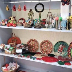 Imagem de prateleiras do Bazar de Natal do Hospital São Vicente, com enfeites natalinos, brinquedos, louças e itens decorativos organizados para venda.