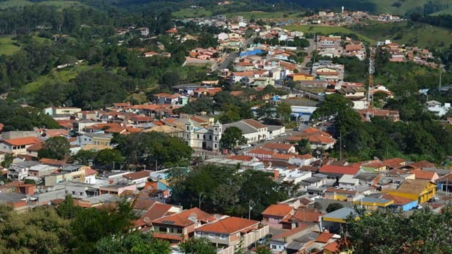Vista aérea de Cabreúva, com casas de telhados vermelhos, uma igreja central e áreas verdes ao fundo, mostrando a integração da cidade com o entorno natural.