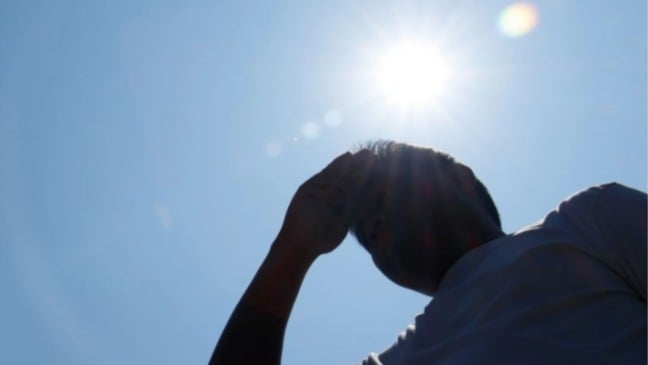 Pessoa se protege do sol sob céu azul durante forte onda de calor.