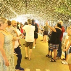 Pessoas caminhando e tirando fotos dentro de um túnel iluminado por milhares de luzes douradas no Natal Encantado de Itupeva.