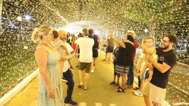 Pessoas caminhando e tirando fotos dentro de um túnel iluminado por milhares de luzes douradas no Natal Encantado de Itupeva.