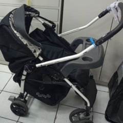 Carrinho de beb&ecirc; esquecido e guardado em &aacute;rea de achados e perdidos, com estrutura met&aacute;lica clara e assento escuro.