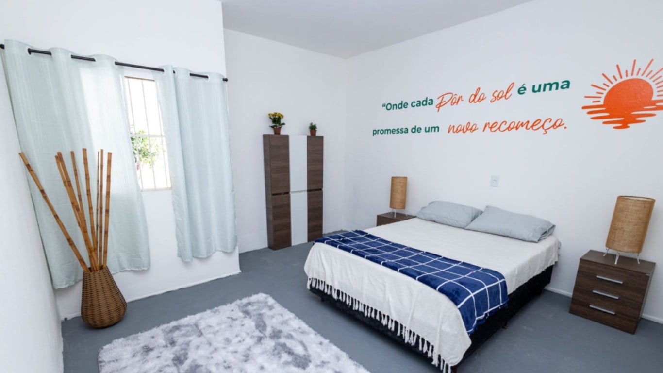 Quarto da Casa da Família com cama de casal, decoração simples e frase motivacional “Onde cada pôr do sol é uma promessa de um novo recomeço” na parede. Quarto da Casa da Família com cama de casal, decoração simples e frase motivacional “Onde cada pôr do sol é uma promessa de um novo recomeço” na parede.
